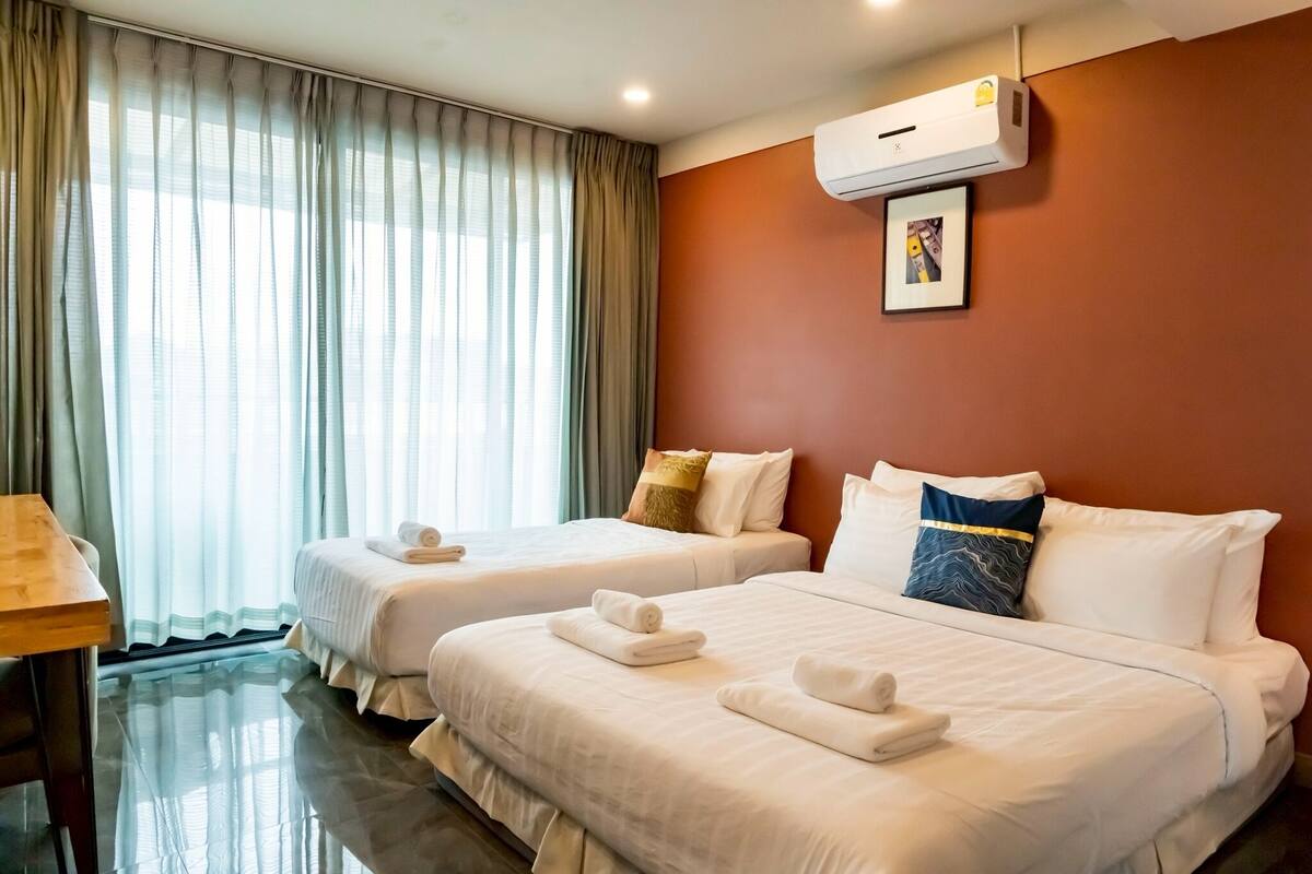 Habitación de hotel con dos camas, una mesa y un equipo de aire acondicionado.
