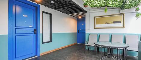 Una habitación con dos puertas azules, una mesa con sillas, una planta colgante y un cuadro enmarcado en la pared.