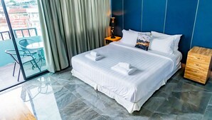 Ein Hotelzimmer mit einem großen Bett, einem Nachttisch aus Holz, einem Glastisch mit Stühlen und Blick auf Gebäude durch das Fenster.