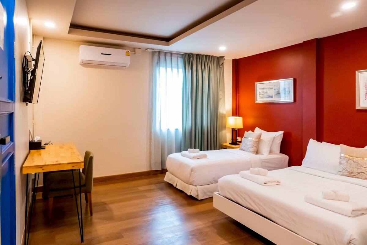 Habitación de hotel con dos camas, un escritorio y una ventana con cortinas.