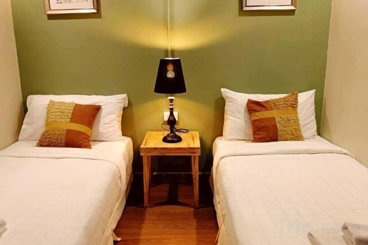 Habitación doble con dos camas, una mesita de noche, una lámpara y un cuadro en la pared.