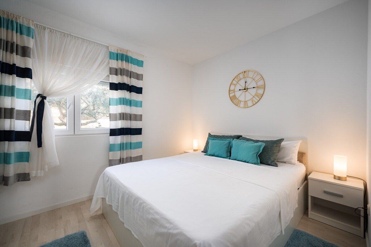Un dormitorio con cama, mesitas de noche, un reloj de pared y cortinas.