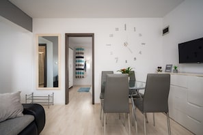 En moderne stue med sofa, spiseområde med stole, et fjernsyn ophængt på væggen og et ur.