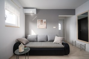 En moderne stue med en grå sofa, et rundt bord og en vægmonteret aircondition.