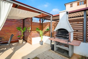 En udendørs terrasse med integreret grill, plantekrukker og et overdækket siddeområde.