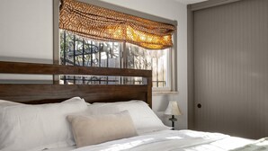 A neatly made bed with white linens and a wooden headboard, a bedside lamp, and a window with patterned curtains. - Private retreat in the heart of Chico, just moments away from the enchanting Lower Bidwell Park (Chico)