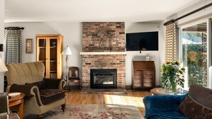 A living room with a fireplace, wooden furniture, and a view through a large window. - Private retreat in the heart of Chico, just moments away from the enchanting Lower Bidwell Park (Chico)