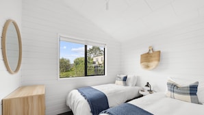 Una camera da letto con due letti, un armadietto in legno, una finestra con vista su vegetazione e un edificio, e un cesto fissato al muro.