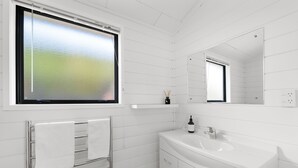 Un bagno moderno con pareti piastrellate di bianco, un ampio specchio, un lavandino bianco e un portasciugamani.