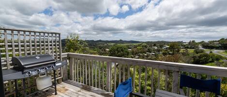 A wooden deck with a grill and chairs, overlooking a scenic landscape.