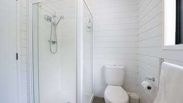 Un baño pequeño y blanco con una ducha de cristal, un inodoro y una toalla colgada en la pared.