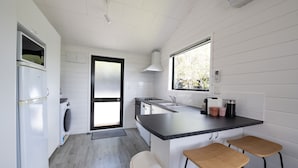 Una cucina funzionale con lavatrice, fornello e lavandino. Sono presenti due sgabelli di legno e una finestra che lascia entrare luce naturale.