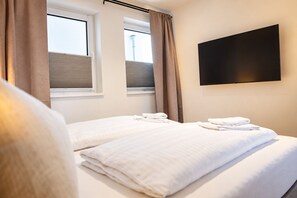 A hotel room with two beds, a flat-screen TV mounted on the wall, and a window with blinds. - Vacation rental (new construction 2023) in prime location with fireplace and bal (Winterberg)