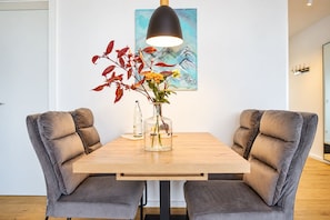 A dining area with a wooden table, two grey upholstered chairs, a clear vase with flowers, and a painting on the wall. - Vacation rental (new construction 2023) in prime location with fireplace and bal (Winterberg)