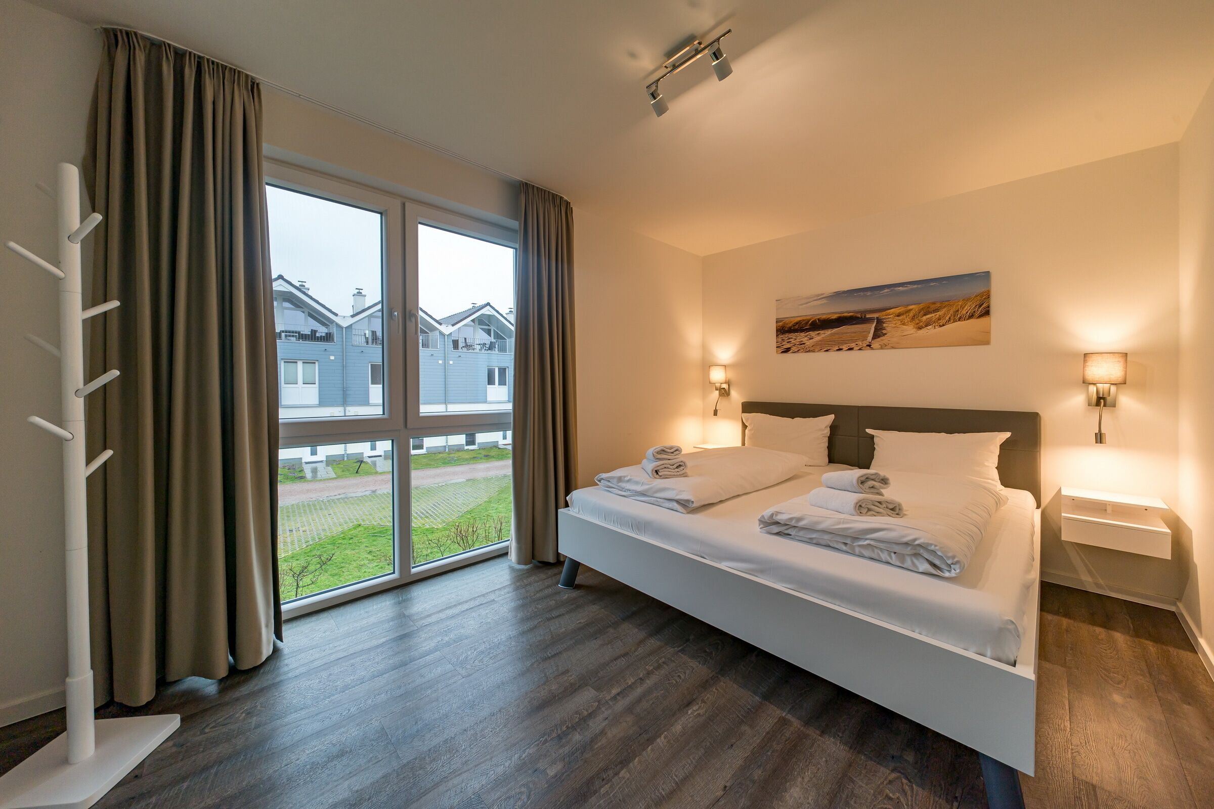 A modern hotel room with a large bed, two bedside tables, a window with curtains, and a view of the outside.