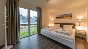 Une chambre d’hôtel moderne avec un grand lit, deux tables de chevet, une fenêtre avec des rideaux et une vue sur l’extérieur.