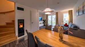 Un salon moderne avec une table à manger en bois, des chaises, une cheminée et un canapé, avec un téléviseur en arrière-plan.