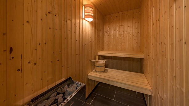 Un sauna en bois, avec un banc, un seau et un plateau rempli de pierres.