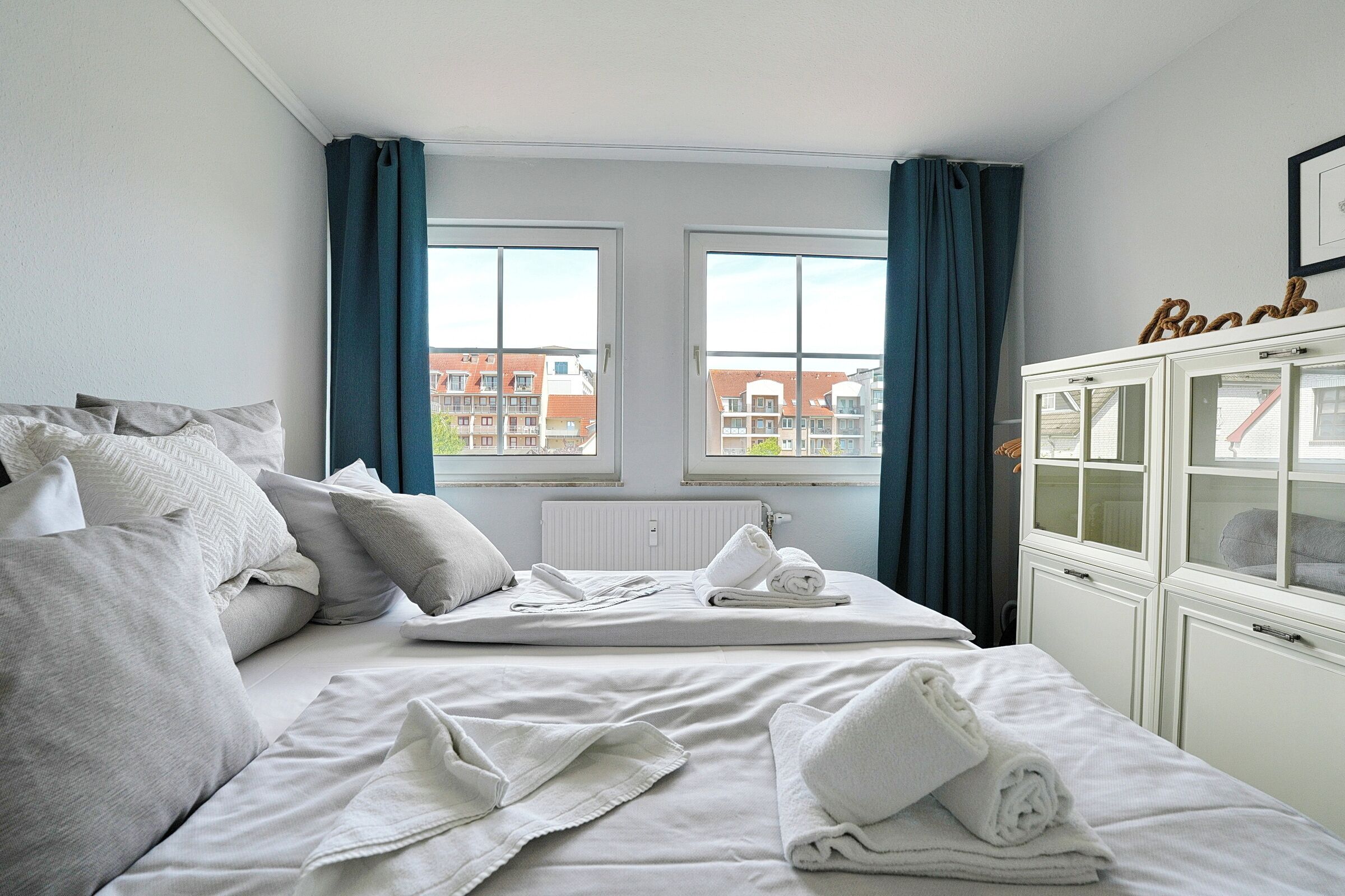 Quarto de hotel com uma cama, duas janelas, um armário e vista para prédios.