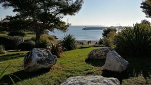 Paisatge costaner amb una zona verda, roques grans i vista al mar.