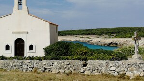 Església blanca amb una torre de campanars, una paret de pedra i una estàtua al primer pla.