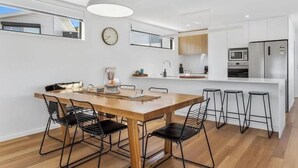 Une cuisine moderne avec une table à manger en bois, des chaises à armature métallique noire, un plan de travail blanc et un réfrigérateur en acier inoxydable.
