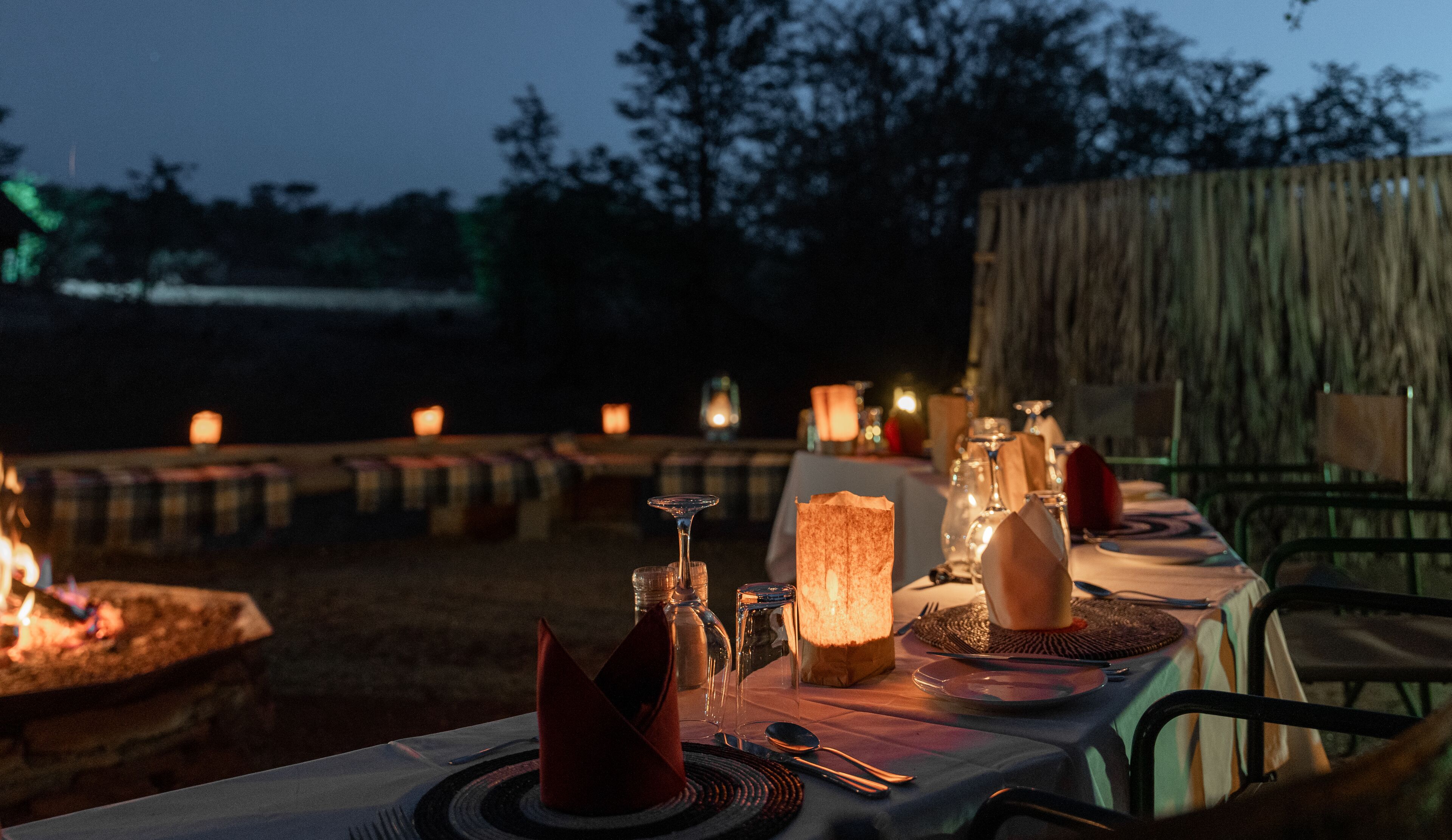 An outdoor dining setup with tables, candles, and a fire pit.