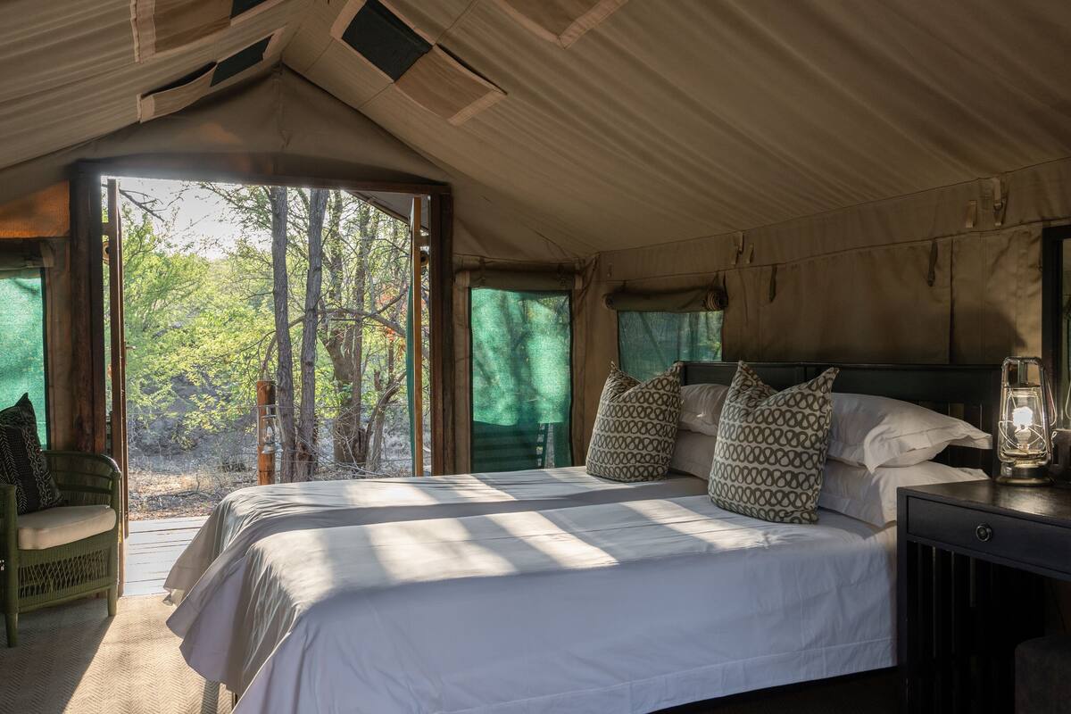 A spacious bedroom with a large bed, a wooden nightstand, a mirror, and a view of the outdoors.