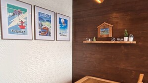 Une pièce avec une table en bois, des affiches encadrées au mur et une étagère ornée de pommes de pin.