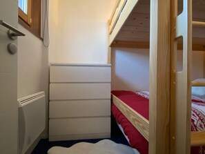 Une petite chambre à coucher avec un lit superposé, une commode blanche et un radiateur.