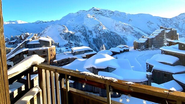 Un village de montagne enneigé, avec des bâtiments en bois et un ciel d’un bleu limpide.