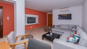 Ein modernes Wohnzimmer mit grauem Sofa, einem Couchtisch und einem an der weißen Wand montierten Fernseher.