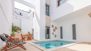 Ein moderner Poolbereich im Freien mit Holzterrasse, Sitzgelegenheiten und einer Treppe zu einer erhöhten Ebene.