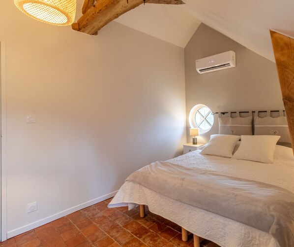 Une chambre à coucher comprenant un lit, une table de chevet, une lampe, un appareil de climatisation et une fenêtre avec un rideau.