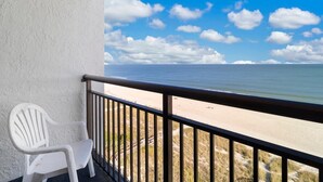 A balcony with a white plastic chair overlooking a beach with a clear sky. - Oceanfront Suite: Complimentary Breakfast 10th Flr (Myrtle Beach)