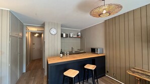A modern kitchen with a wooden island, two bar stools, a hanging light fixture, and a clock on the wall. - Bright studio in Pra-Loup with private parking, close to slopes (Pra-Loup)