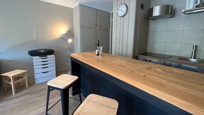 A modern kitchen with a wooden island, two bar stools, a built-in oven, and a clock on the wall. - Bright studio in Pra-Loup with private parking, close to slopes (Pra-Loup)