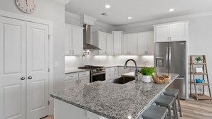 A modern kitchen with white cabinetry, a granite countertop, stainless steel appliances, and a clock on the wall.