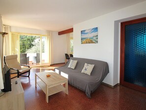 A room with a sofa, a table, and a chair. There is a window with curtains, a painting on the wall, and a door with a glass panel. - Spacious Villa with Garden Near the Beach (Llançà)