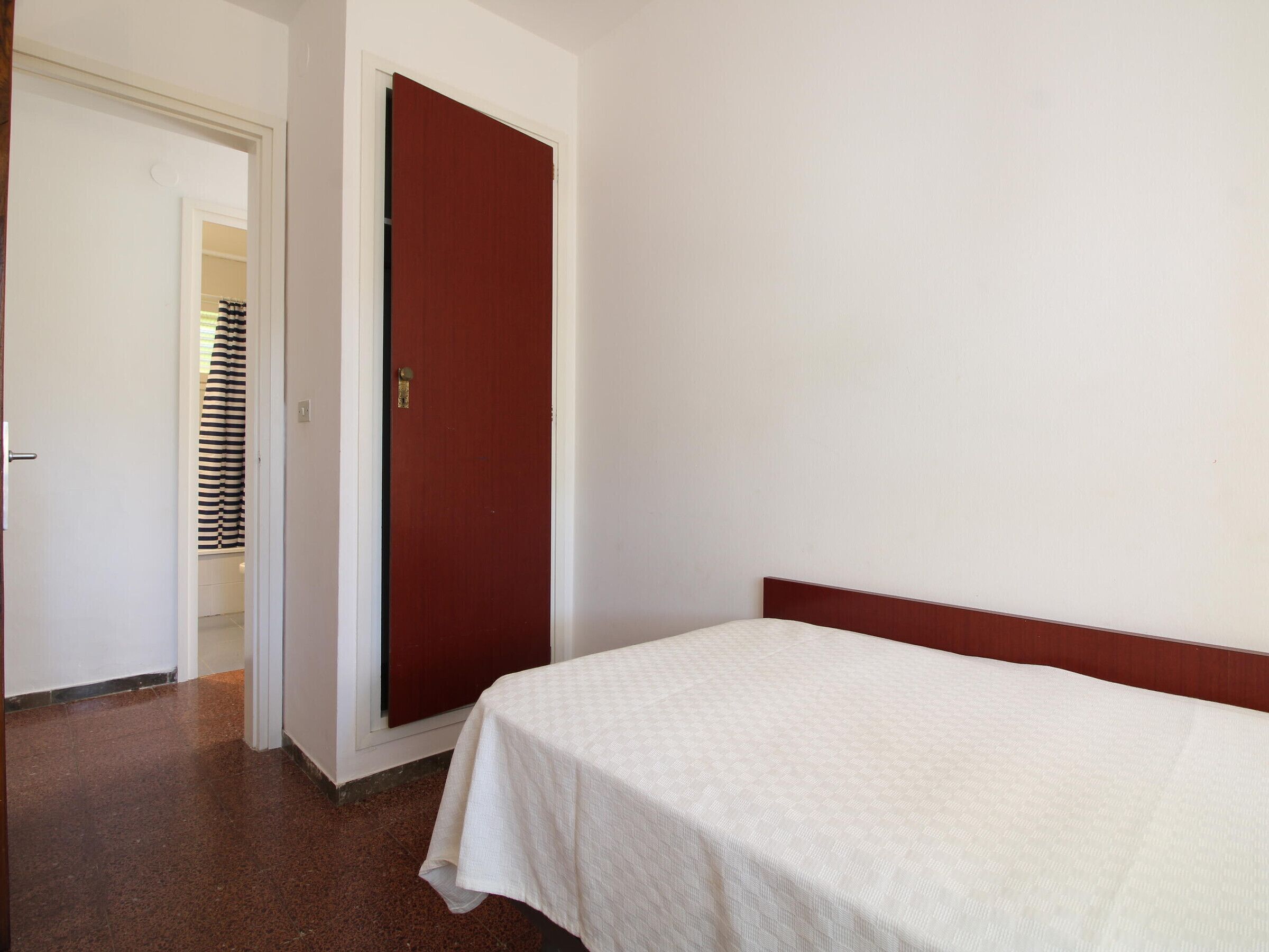 A room with a single bed, a red door, and a white wall.