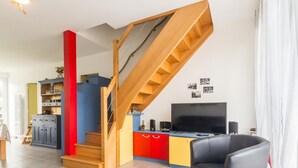 Ein modernes Wohnzimmer mit einer Holztreppe, einem Flachbildfernseher und einem schwarzen Ledersofa.