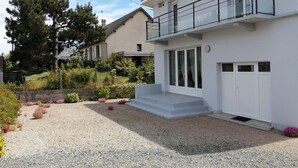 Ein modernes, zweistöckiges Haus mit Balkon, einem Schotterweg und einem Garten mit verschiedenen Pflanzen und Blumen.