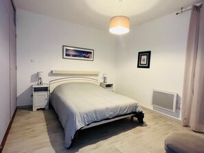 Une chambre à coucher avec un lit, des tables de chevet, une lampe, un tableau au mur et un radiateur.