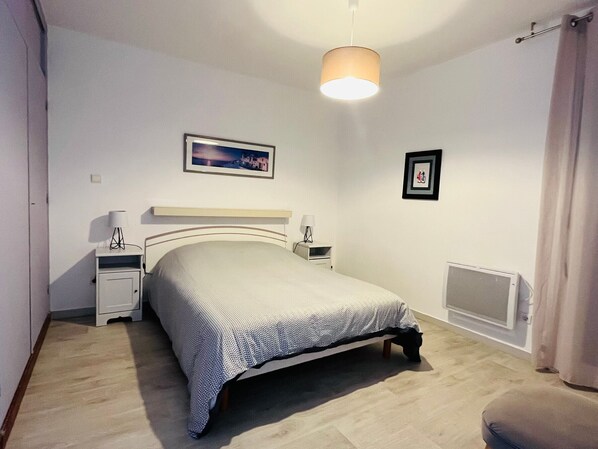 Une chambre à coucher avec un lit, des tables de chevet, une lampe, un tableau au mur et un radiateur.