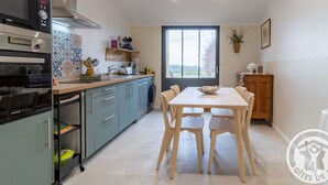 Cocina moderna con horno empotrado, microondas y lavavajillas. Hay una mesa de comedor con cuatro sillas y una ventana que ofrece vistas al exterior.
