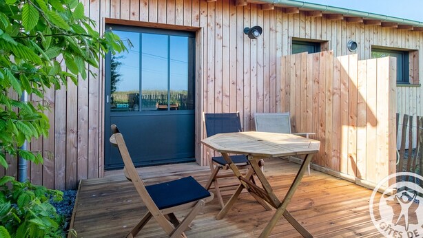 Una terraza de madera con una mesa, sillas, una puerta corrediza y vistas al exterior.