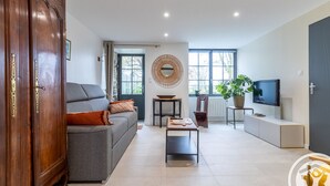 Una sala de estar con sofá, mesa de centro y televisor. Hay un mueble de madera y un espejo grande en la pared.