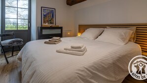 Un dormitorio con una cama grande, cabecera de madera, ventana con vistas, mesita de noche con lámpara y una silla.