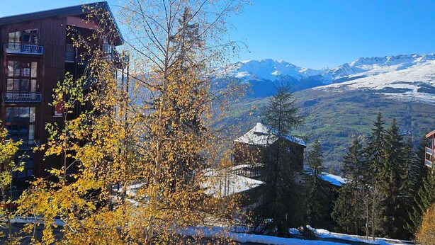 A building with a balcony, surrounded by autumn foliage and a mountain backdrop.