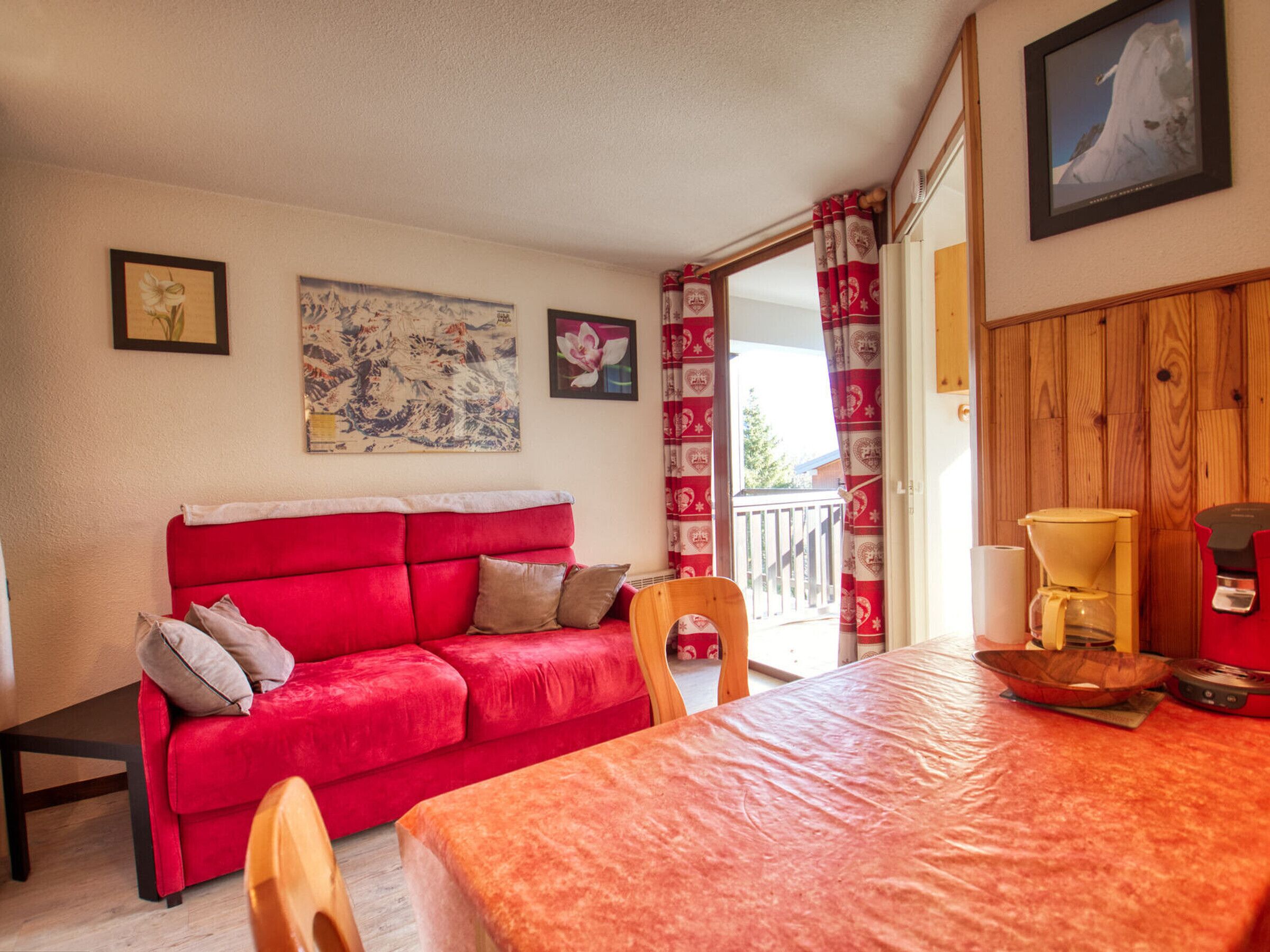 A room with a red sofa, wooden dining table, and a coffee maker.